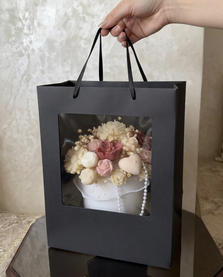 La composition Rose Naissance présentée dans un sac cadeau noir à fenêtre.