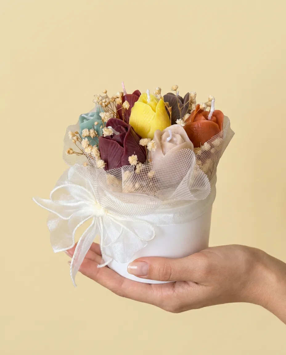 Bouquet de tulipes en cire multicolores dans un pot blanc noué d'un ruban organza, tenu à la main.